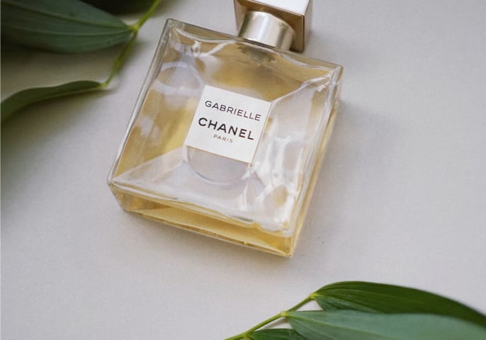 a bottle of Gabrielle Essence Eau de Parfum surrounded by leaves